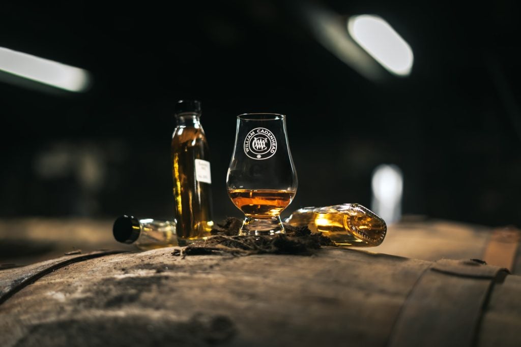 A Cadenhead's bottle and a filled Glencairn glass resting on a cask in the dunnage warehouse