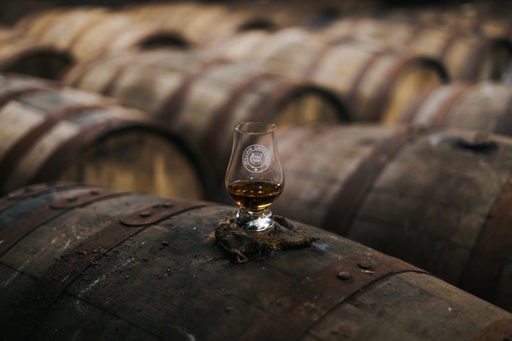 A glass of whisky resting on a cask in the warehouse